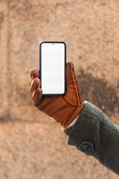 Hand in leather glove holding smartphone with blank white screen