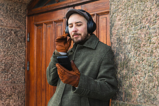Man in winter coat using smartphone with headphones outdoors.