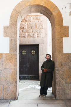 tylish man with headphones leaning against a stone archway in winter.