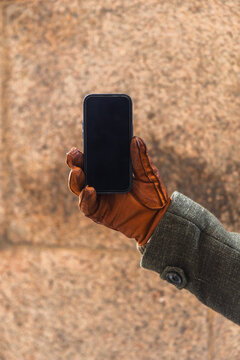 Hand in leather glove holding smartphone with blank black screen