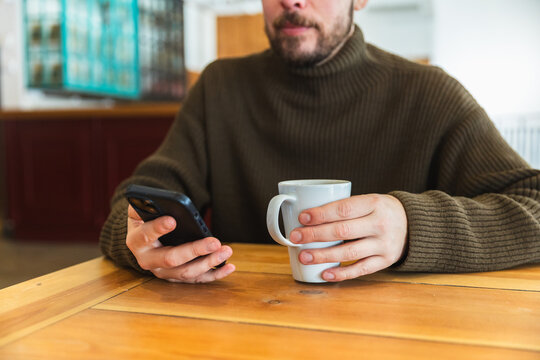 Man using smartphone and drinking coffee in a modern cafe