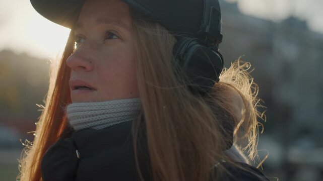 White woman with headphones outdoors, pensive winter closeups showing visible breath, rim light on red hair, scarf and cap, city street background, quiet contemplative mood, slow cinematic frames