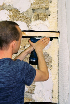 Man screws the board to the wall using a screwdriver.
