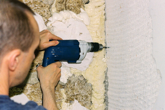 Man drilling a hole in the wall with an electric drill.