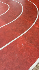 Fototapeta premium Red track curves gracefully under white lines. Freshly painted, the surface gleams with motion. Runner's path, quiet and ready for stride. Ideal for sports, fitness, or athletic training themes.