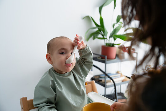 Funny moment of young kid eating with spoon at home