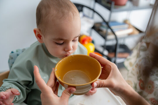 Caring hands helping a young kid drink soup carefully