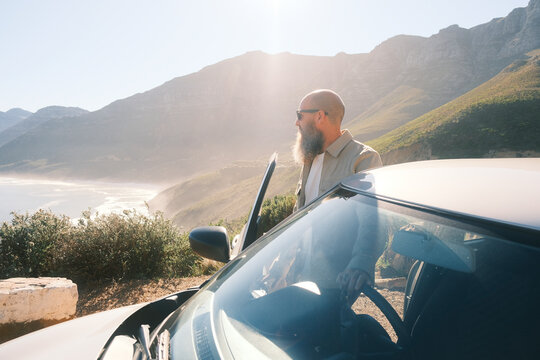 Bearded man wearing sunglasses standing behind car in Cape Town
