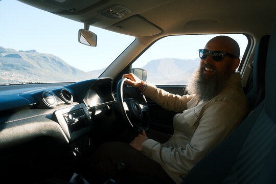 Bearded man driving car along coastal road in Cape Town