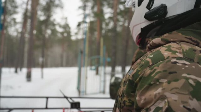 Camouflage rider with white helmet prepares for ride, gripping handlebars of atv and scanning quiet pine forest, snowcovered trail ahead, muted winter light and focused anticipation