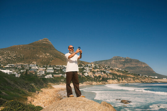 Bearded man taking photo of coastal landscape in Cape Town
