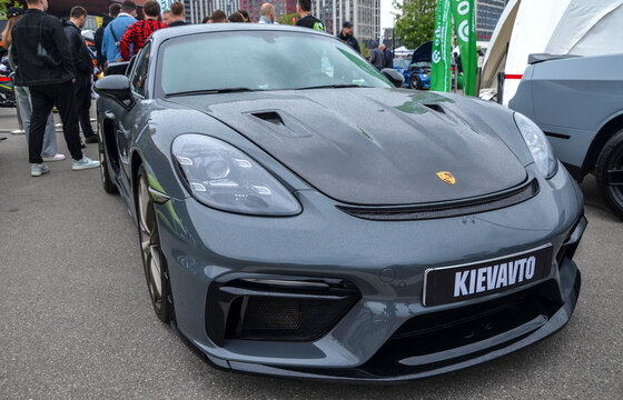 Grey Porsche 718 Cayman GT4 RS with yellow brake calipers and large rear wing is showcased at outdoor event. High-performance German track weapon with aggressive aero