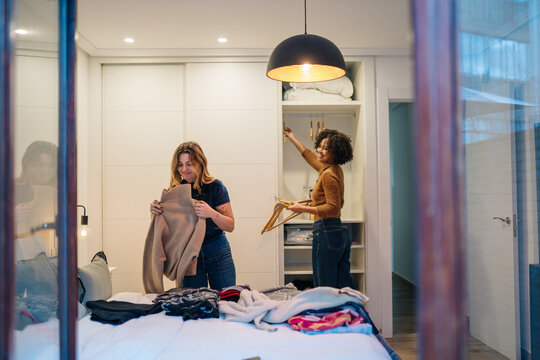 Friends organizing clothes in bedroom closet together