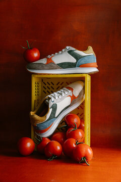 Still life of colourful sneakers and tomatoes on red background