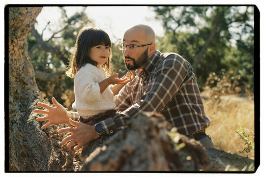 Playful father and daughter on oak tree trunk
