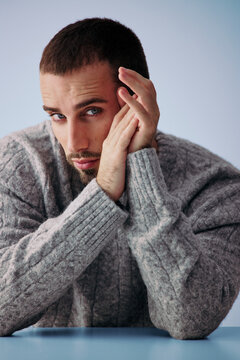 Man Poses With Hands on Face Wearing Gray Sweater Indoors