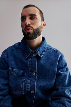 Man Sitting in Denim Jacket Against Simple Background