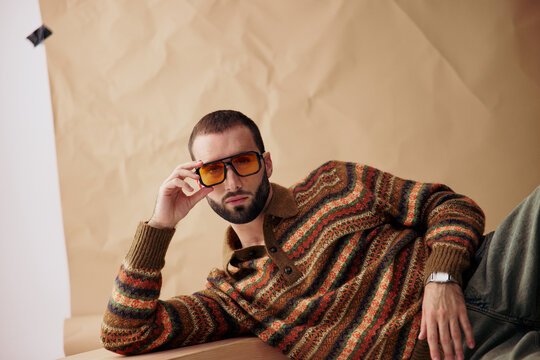 Man Poses in Retro Sweater With Sunglasses Against Brown Backdrop