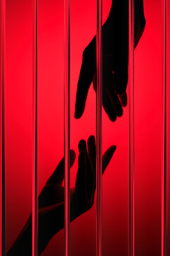 Hands Reaching Each Other behind the glass against a Red Background