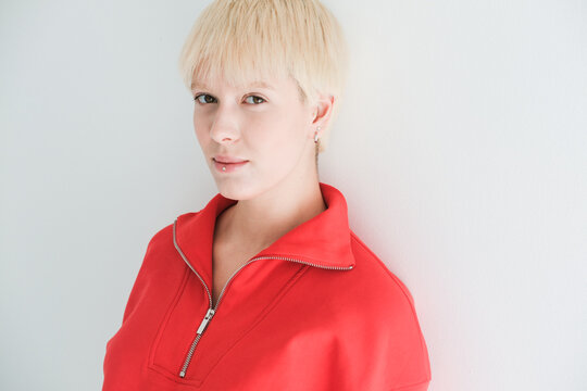 Young Person in Red Top Stands Against White Wall