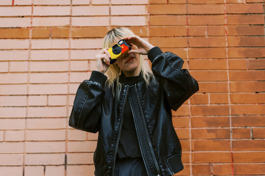 Person Takes Photo in Front of Brick Wall During Daylight