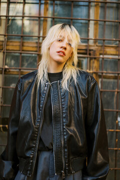 Young Woman Poses in a Black Jacket by a Metal Grate