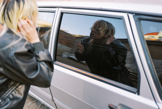Woman Looks at Reflection in Car Window in Urban Area