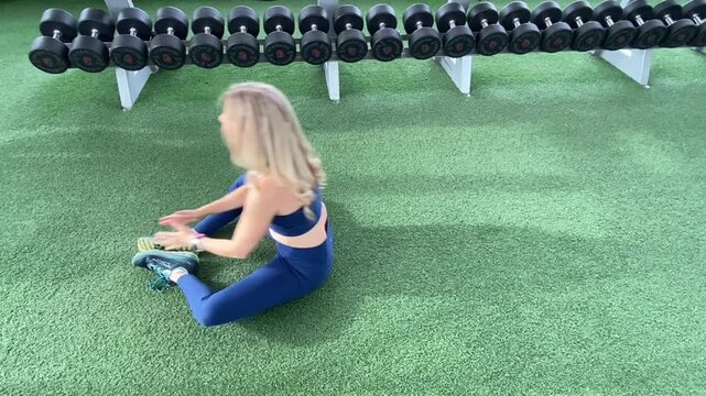 blonde woman doing sit-ups on green turf next to dumbbell weights