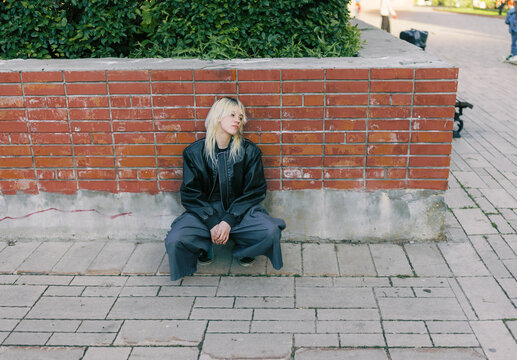 Person Sits Against a Brick Wall in a Public Space During the Day
