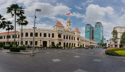 Obraz premium Panoramic perspective of Ho Chi Minh City People's Committee building with surrounding streets, palm trees, and modern skyline blending historic and contemporary architecture.