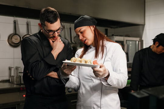 Female Chef Presenting Sushi Plate To Colleague In Kitchen