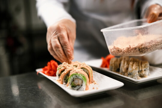 Chef Garnishing Sushi Roll With Crispy Topping