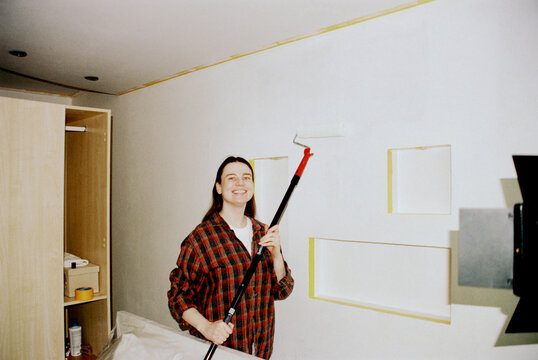 Smiling Brunette Painting Wall With Roller During Renovation
