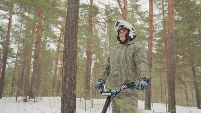 White guide on atv in forest leading winter trail, camo outerwear, helmet and headlight beam, tracked vehicle carving snow, confident stance, scenic pine backdrop, energetic offroad momentum