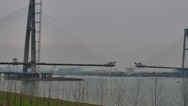 JIANGSU, CHINA - APRIL 17 2026: Construction of a massive cable stayed bridge across the river showing incomplete deck sections and a tall concrete pylon.