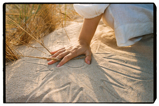 Woman touching sun drawing in sand