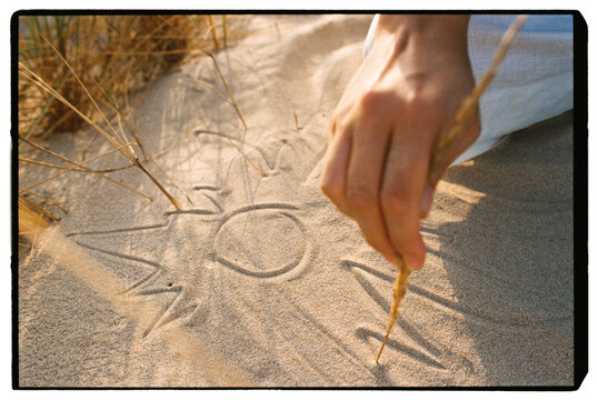 Female hand drawing sun symbol on sand