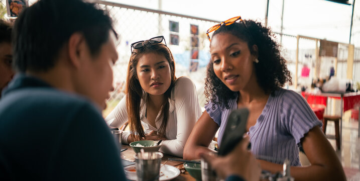 Diverse friends enjoying meal and sharing content on smartphone 