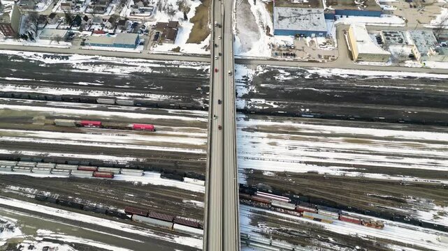 Drone shot following a car as it exits a long bridge over a train yard in winter