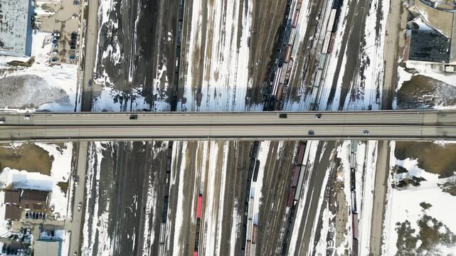 Top down drone shot of a large highway bridge spanning beside a snowy train yard