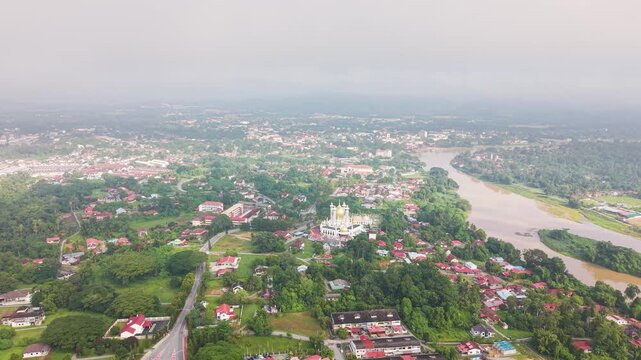 Push in drone shot of Kuala Kangsar in Perak, Malaysia, featuring Ubudiah Mosque surrounded by lush greenery and Sungai Perak river landscape in soft atmospheric conditions. UHD.