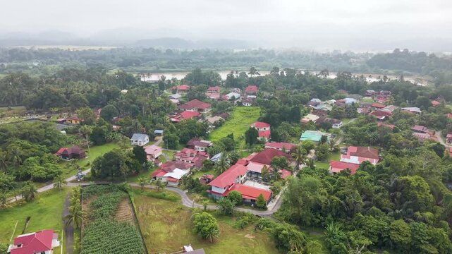 Push in aerial shot of rural village outskirts near Kuala Kangsar, Perak, Malaysia, showing houses, greenery, river landscape, and peaceful countryside environment in tropical Southeast Asia. UHD.