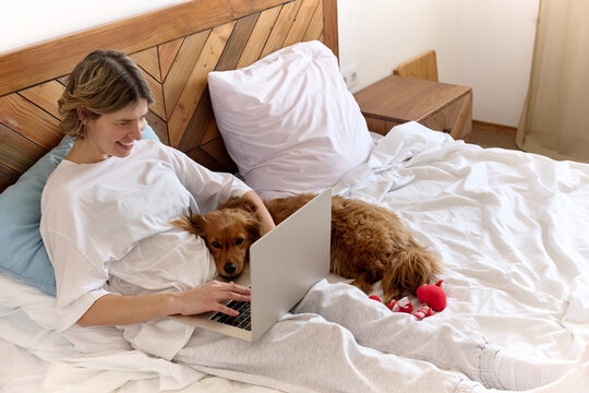 Woman Using Laptop in Bed with Pet Dog