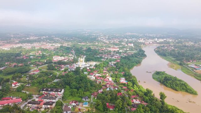 Expansive aerial shot of Kuala Kangsar in Perak, Malaysia, featuring Ubudiah Mosque surrounded by lush greenery and Sungai Perak river landscape in soft atmospheric conditions. UHD.