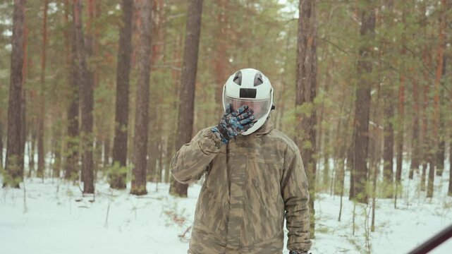 White man prepping red atv in snowy pine forest, scout signaling like forest ranger, inspecting engine and gear, mounting vehicle in camouflage and helmet, starting throttle and driving