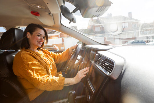Smiling woman inside car touching radio buttons 