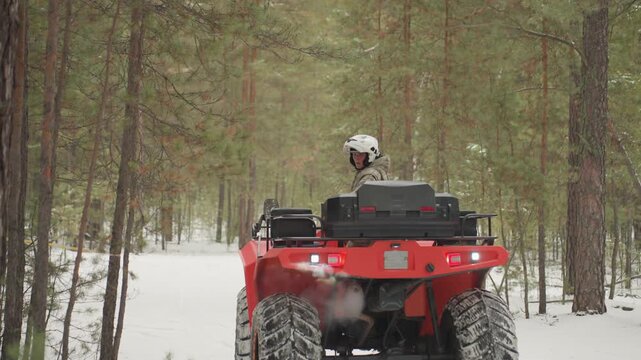 Red atv on snowy forest trail front view with rider in white helmet standing, engine steam and headlights visible, tires gripping snow between pines, steady exploration vibe, offroad extreme journey