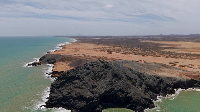 Spectacular drone video sweeps over Pil&oacute;n de Az&uacute;car in Cabo de la Vela, revealing dramatic rocky hills, arid desert, turquoise coastline, and vast skies in sunlit La Guajira. Stunning aerial footage.