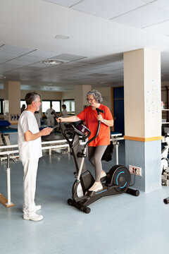 Senior woman exercising on elliptical machine with physiotherapist