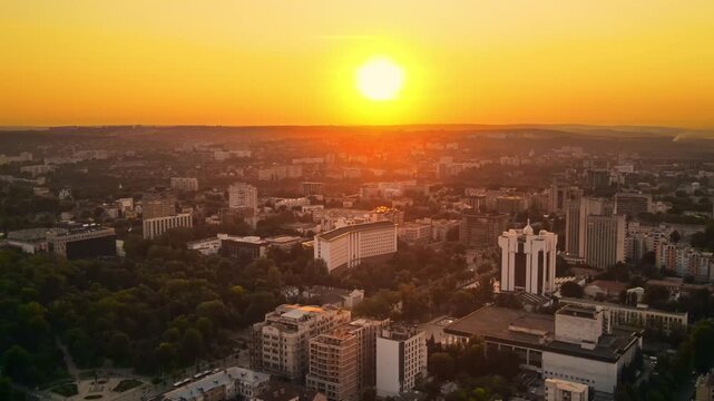 Chisinau city panorama at vibrant sunset with buildings and green trees, sun disk on horizon motion.